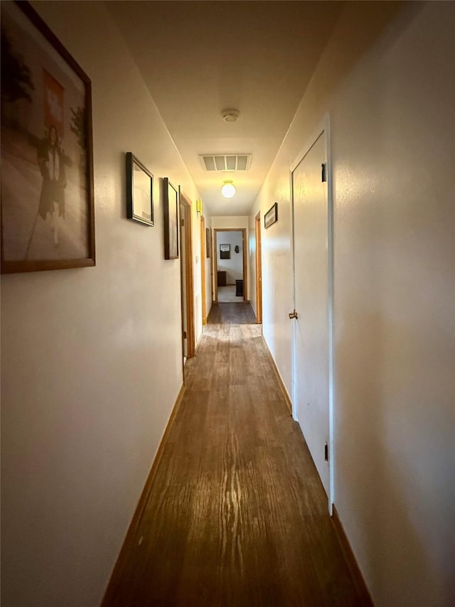 hallway featuring wood finished floors, visible vents, and baseboards
