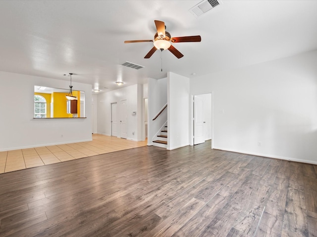 unfurnished living room featuring wood finished floors, visible vents, ceiling fan, and stairs