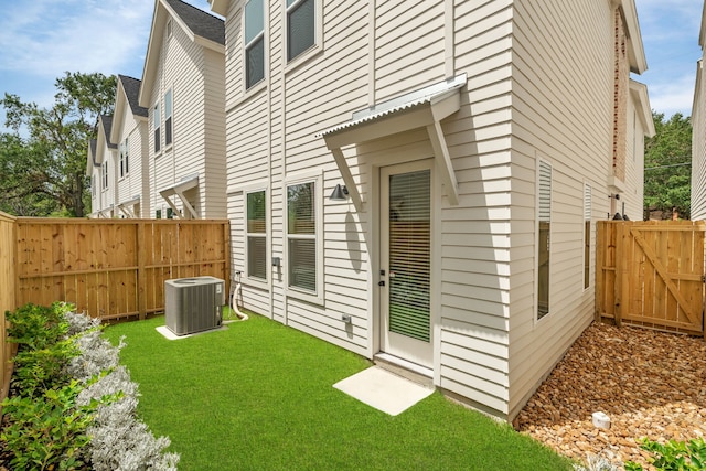 back of property with a shingled roof, fence private yard, cooling unit, and a lawn