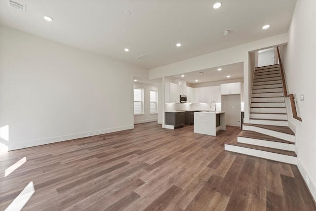 unfurnished living room with stairs, a sink, wood finished floors, and visible vents