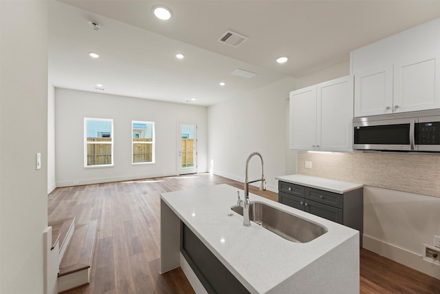 kitchen featuring tasteful backsplash, stainless steel microwave, white cabinets, a sink, and dark wood-type flooring