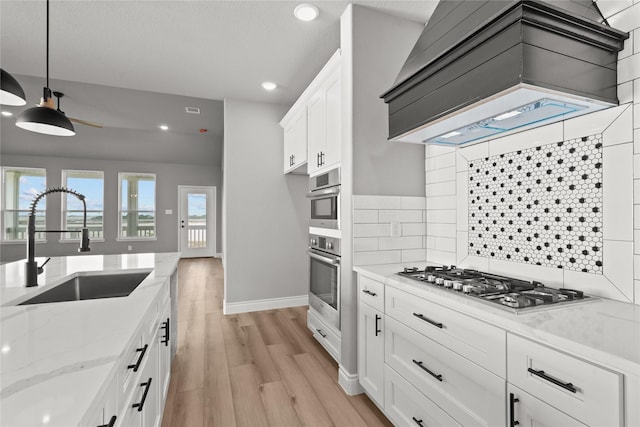 kitchen featuring recessed lighting, stainless steel gas stovetop, light wood finished floors, a sink, and premium range hood