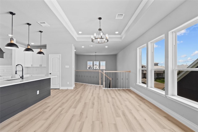 kitchen with a sink, light countertops, a tray ceiling, an inviting chandelier, and light wood-type flooring