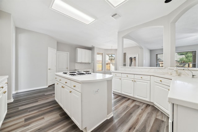 kitchen featuring arched walkways, wood finished floors, a kitchen island, white gas stovetop, and visible vents
