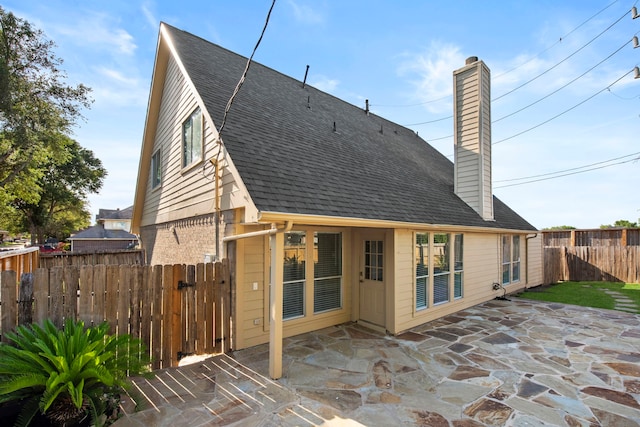 back of house with a chimney, fence, roof with shingles, and a patio area