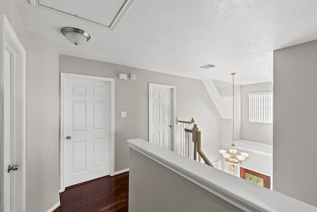 corridor with an upstairs landing, dark wood-type flooring, visible vents, baseboards, and a textured ceiling