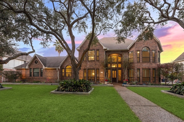 tudor house featuring roof with shingles, a yard, and brick siding