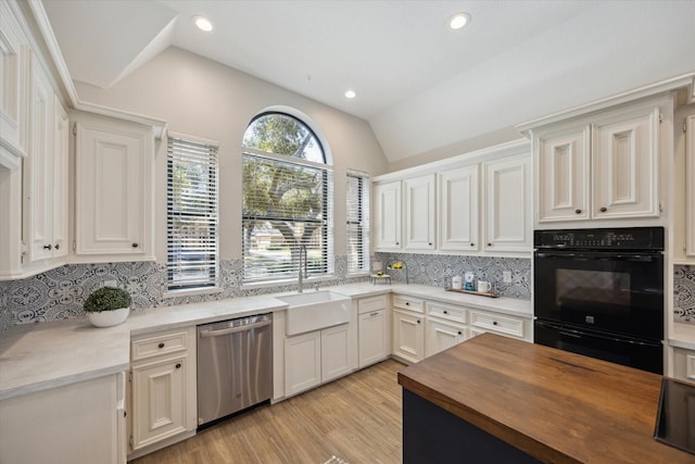 kitchen with stainless steel dishwasher, butcher block countertops, light wood-style floors, vaulted ceiling, and a sink