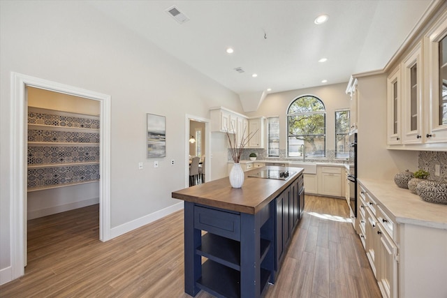 kitchen featuring blue cabinetry, light wood-style flooring, decorative backsplash, butcher block counters, and open shelves
