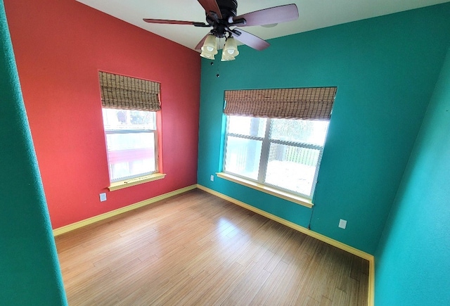 spare room with wood finished floors, a healthy amount of sunlight, a ceiling fan, and baseboards