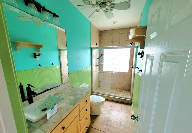 bathroom featuring a shower stall, ceiling fan, a wainscoted wall, toilet, and vanity