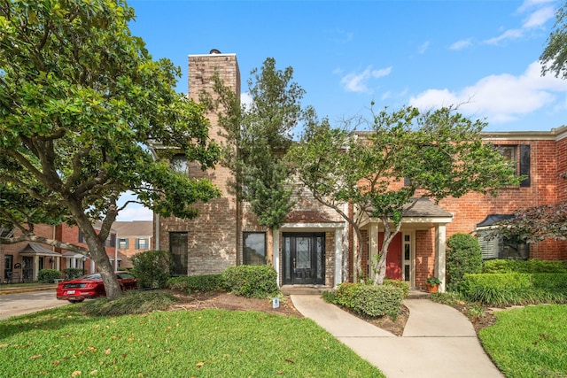 view of property featuring brick siding, a chimney, and a front yard