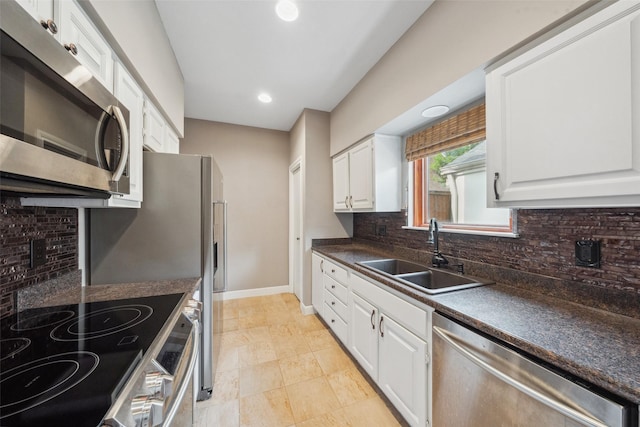 kitchen featuring dark countertops, appliances with stainless steel finishes, a sink, white cabinetry, and tasteful backsplash