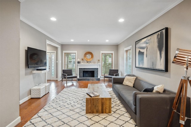 living area with a fireplace with raised hearth, recessed lighting, baseboards, wood finished floors, and ornamental molding