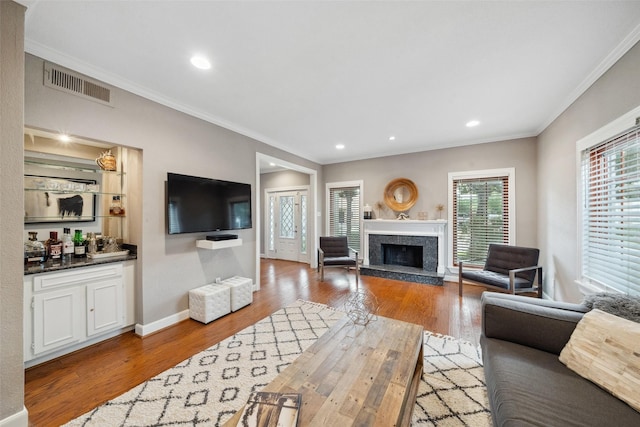 living area with a fireplace, recessed lighting, wood finished floors, visible vents, and ornamental molding