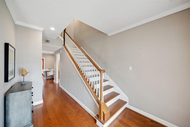staircase with baseboards, ornamental molding, wood finished floors, and visible vents