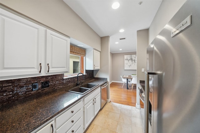 kitchen with white cabinets, dark countertops, appliances with stainless steel finishes, a sink, and decorative backsplash