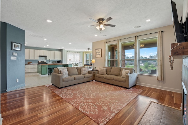 living area featuring light wood-style floors, a ceiling fan, a textured ceiling, and visible vents