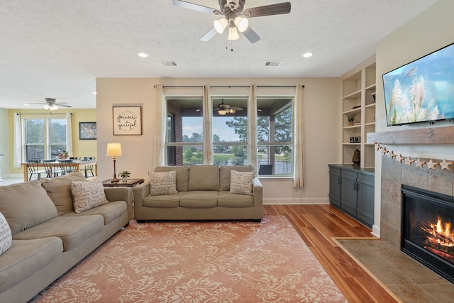 living area with a fireplace, a textured ceiling, a ceiling fan, recessed lighting, and light wood-type flooring