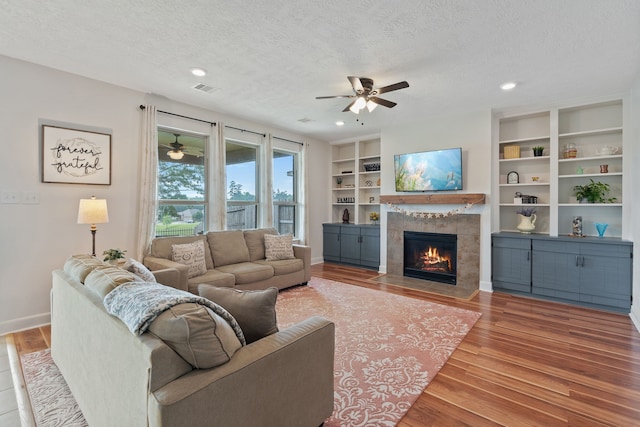 living room featuring visible vents, wood finished floors, a textured ceiling, a tile fireplace, and a ceiling fan