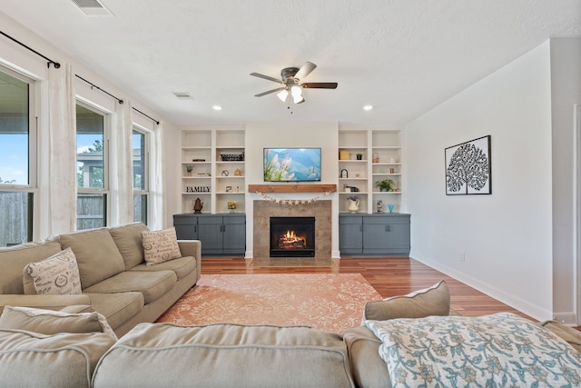 living room with visible vents, wood finished floors, baseboards, a tiled fireplace, and a ceiling fan