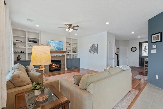 living room featuring ceiling fan, a fireplace, built in features, recessed lighting, and baseboards
