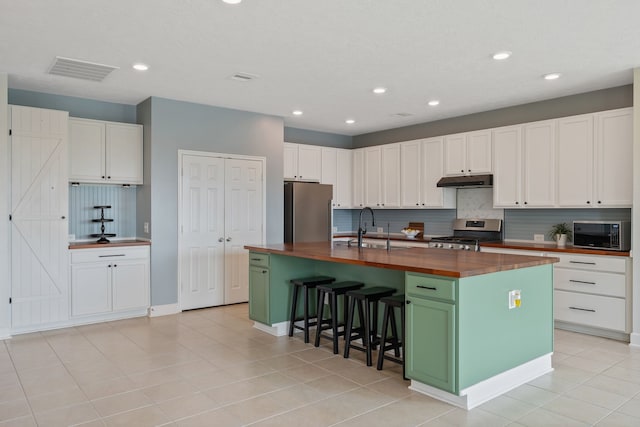 kitchen with decorative backsplash, stainless steel appliances, butcher block counters, and under cabinet range hood