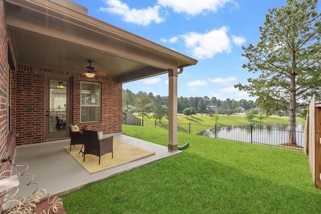 view of yard with a water view, ceiling fan, a fenced backyard, and a patio area