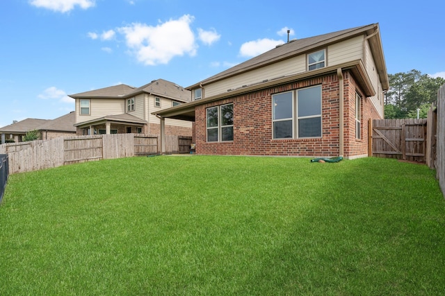 rear view of property featuring a lawn, a fenced backyard, and brick siding