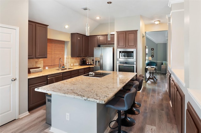 kitchen featuring a sink, stainless steel appliances, vaulted ceiling, wood finished floors, and a kitchen island with sink