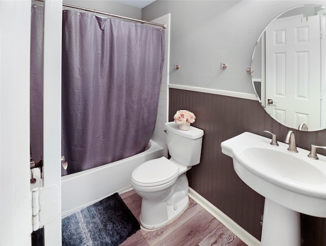 full bathroom featuring shower / bath combo, a sink, a wainscoted wall, toilet, and wood finished floors