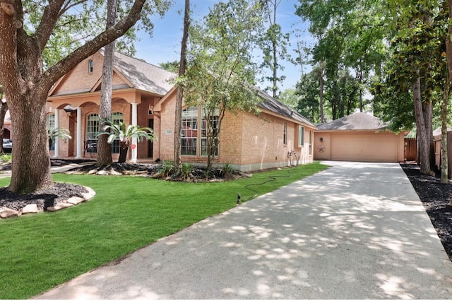 view of front facade with a garage, a front yard, brick siding, and an outbuilding