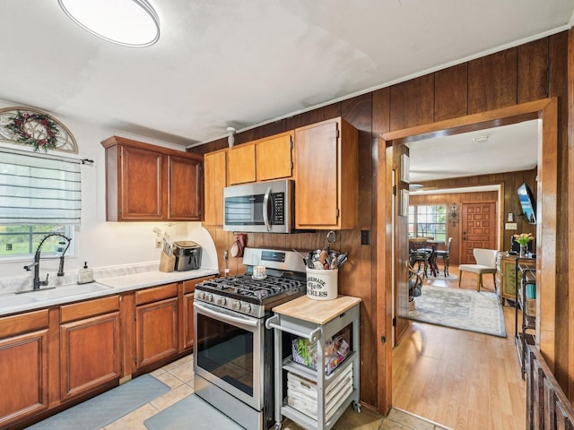 kitchen with brown cabinets, a sink, stainless steel appliances, wood walls, and light countertops