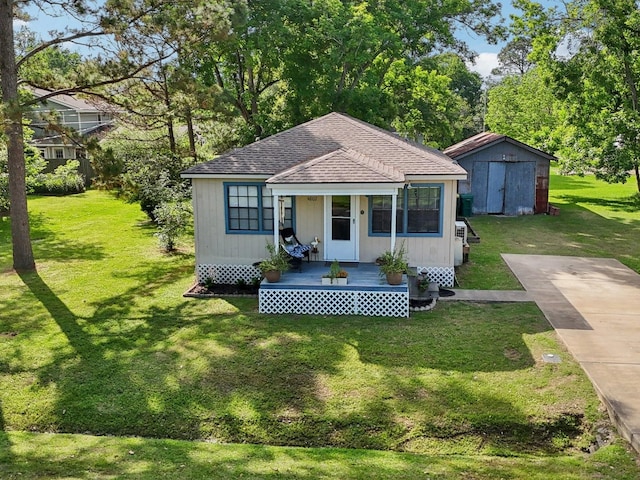 bungalow with roof with shingles, covered porch, a front lawn, and an outbuilding