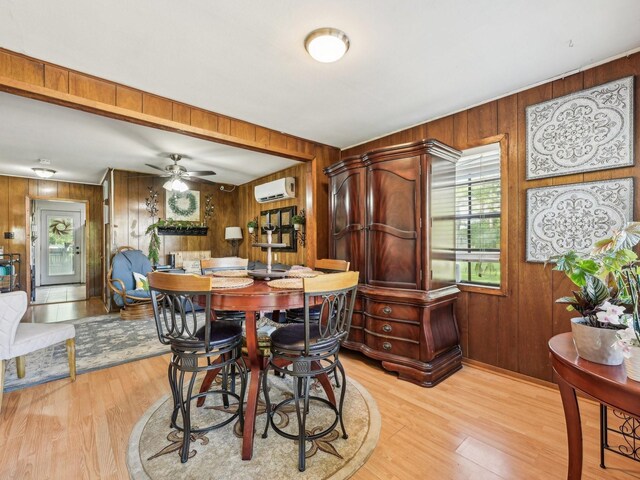 dining room featuring wooden walls, ceiling fan, a wall unit AC, and light wood-style flooring