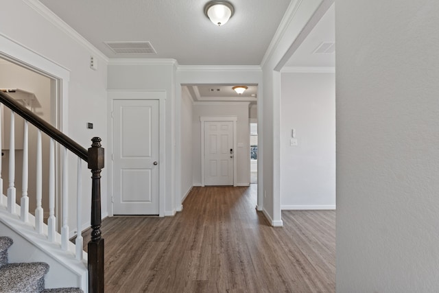 foyer entrance with visible vents, baseboards, crown molding, and wood finished floors