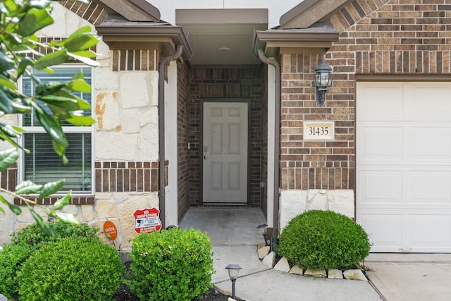 doorway to property with a garage, stone siding, and brick siding