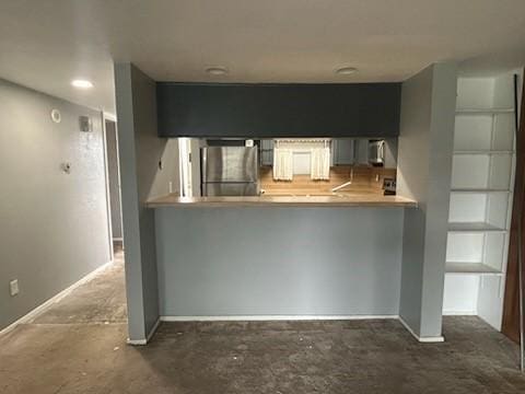 kitchen featuring a peninsula, carpet flooring, freestanding refrigerator, and baseboards