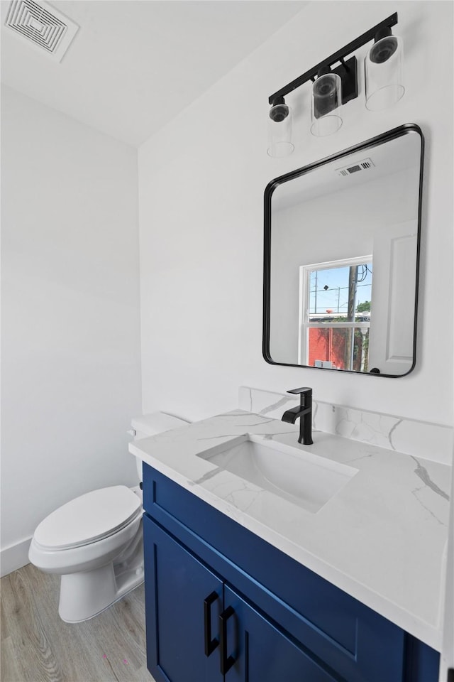 half bath with toilet, wood finished floors, visible vents, and vanity