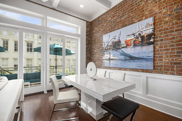 dining space featuring brick wall, beamed ceiling, a wainscoted wall, dark wood-style flooring, and crown molding