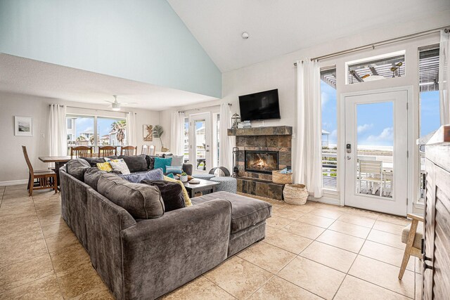 living area with high vaulted ceiling, light tile patterned floors, a ceiling fan, and a stone fireplace