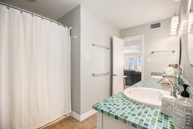 bathroom featuring vanity, visible vents, a textured ceiling, baseboards, and tile patterned flooring