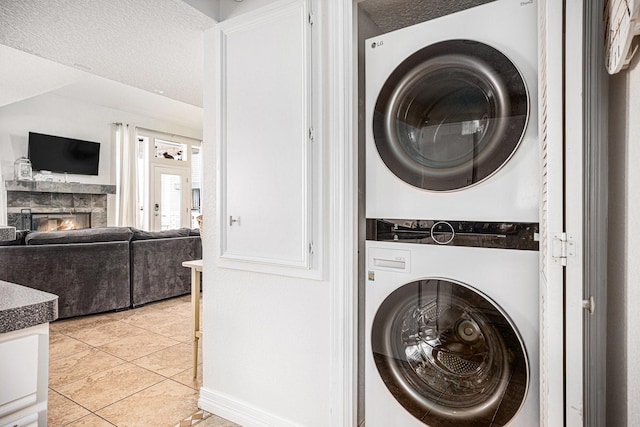 laundry area featuring stacked washing maching and dryer, a fireplace, light tile patterned floors, laundry area, and a textured ceiling