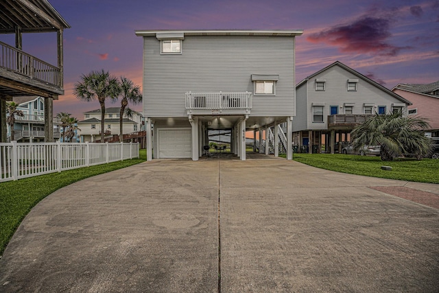 back of property at dusk featuring a balcony, a carport, driveway, an attached garage, and fence