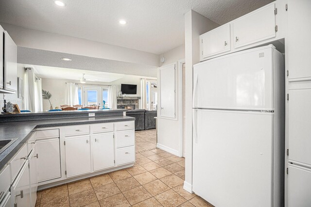 kitchen with a fireplace, light tile patterned flooring, dark countertops, white cabinets, and freestanding refrigerator