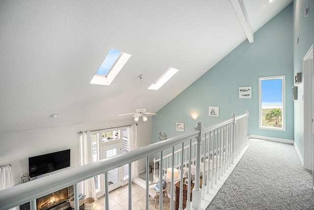hallway with an upstairs landing, a skylight, high vaulted ceiling, and a healthy amount of sunlight