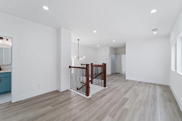empty room featuring visible vents, a notable chandelier, light wood-style flooring, and baseboards