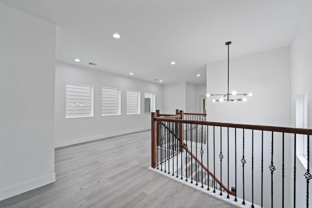 hall featuring light wood-style flooring, an upstairs landing, visible vents, baseboards, and an inviting chandelier