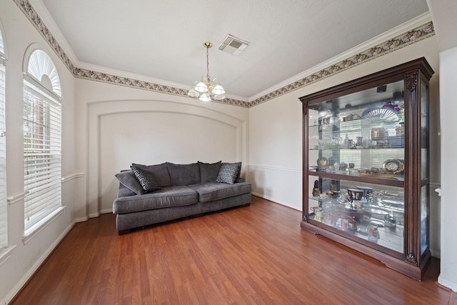 living area featuring visible vents, ornamental molding, an inviting chandelier, wood finished floors, and baseboards