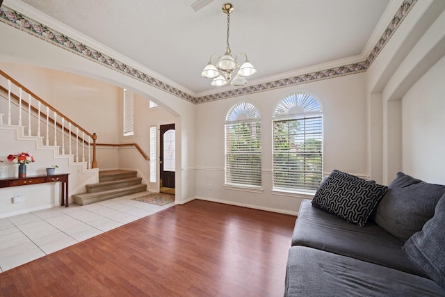 living room with crown molding, arched walkways, wood finished floors, an inviting chandelier, and stairs